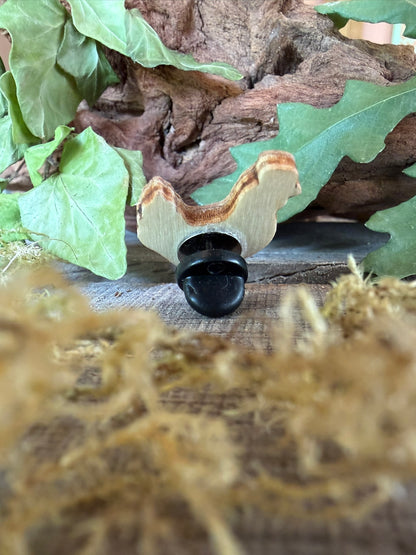 Reverse of the white chicken cork pin badge on weathered wood showing FSC ply base layers and black rubber butterfly clasp, driftwood and oak leaves backdrop