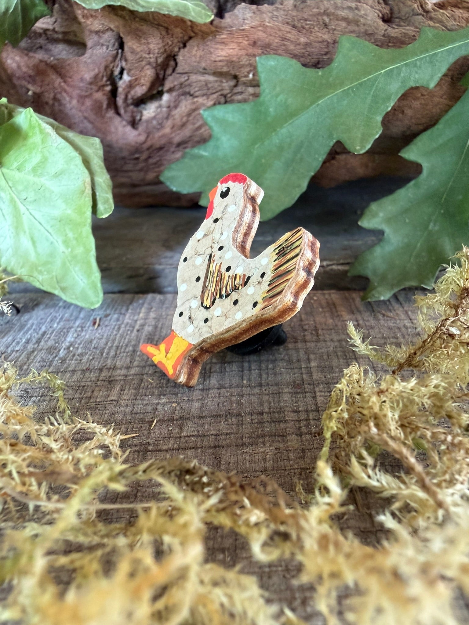 Side profile of the white chicken cork pin badge on weathered wood with driftwood and dried moss — showing cork layers and FSC ply base