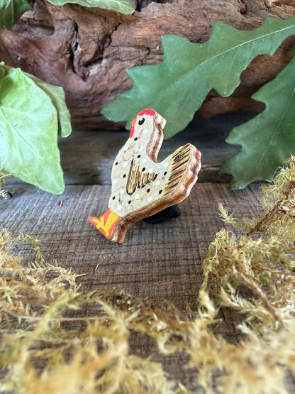 Side profile of the white chicken cork pin badge on weathered wood with driftwood and dried moss — showing cork layers and FSC ply base
