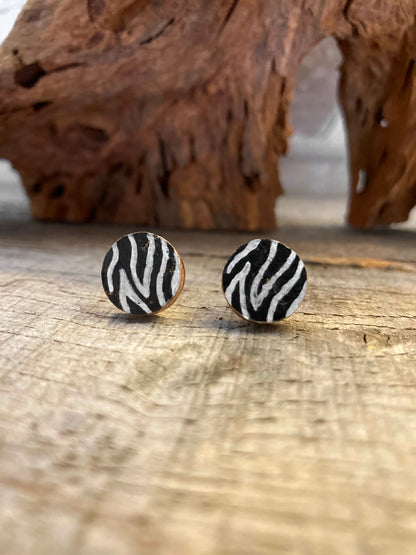 Handpainted zebra print cork stud earrings with bold black and white stripes on a driftwood surface