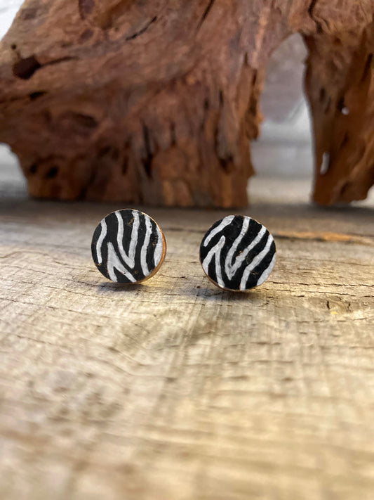 Handpainted zebra print cork stud earrings with bold black and white stripes on a driftwood surface